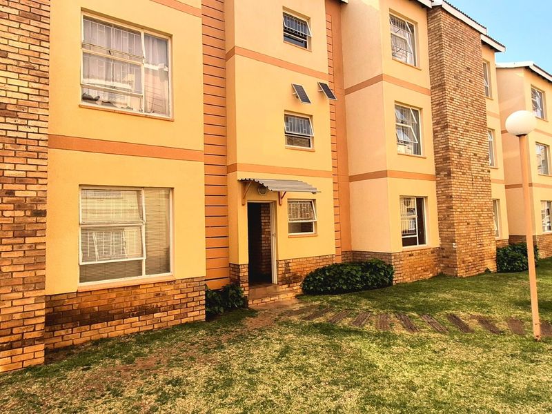 Exterior view of a multi-story apartment building featuring a combination of face brick and plastered finishes with established lawn area.