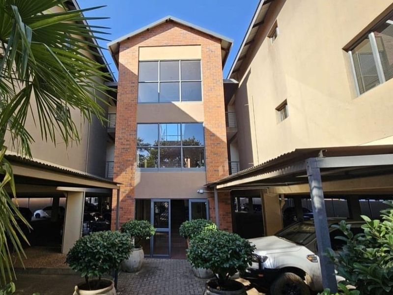 Front elevation of a multi-story apartment complex featuring a brick facade, glass entrance, and covered parking bays.