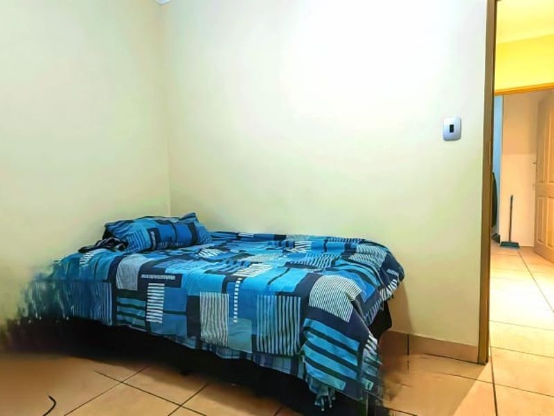 A bedroom featuring tiled flooring and neutral walls, with an adjacent hallway visible through the doorway.