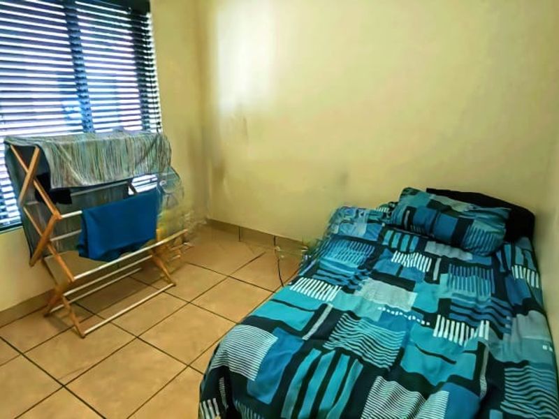 A compact bedroom featuring tiled flooring and venetian blinds, currently showing signs of wear on the walls.