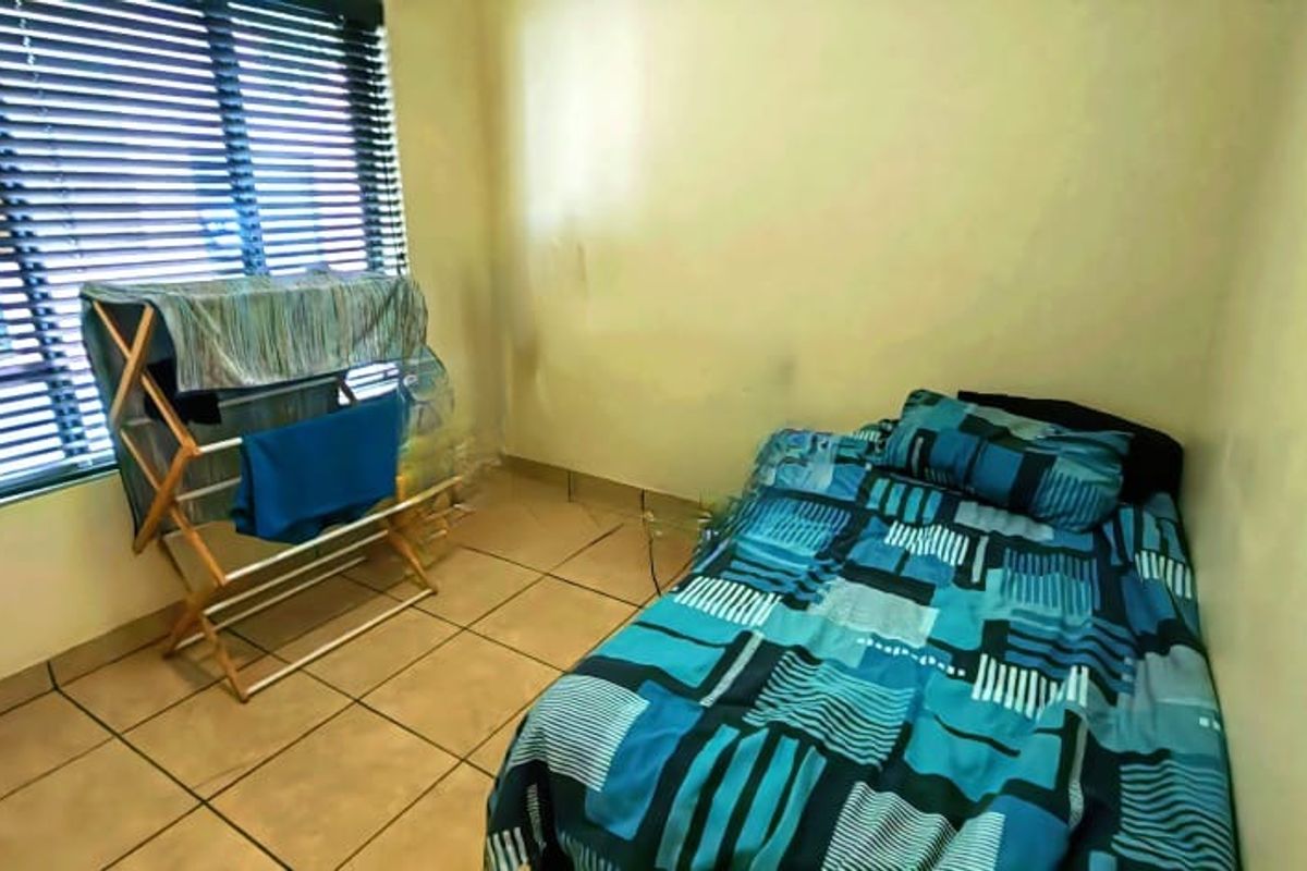 A compact bedroom featuring tiled flooring and venetian blinds, currently showing signs of wear on the walls.