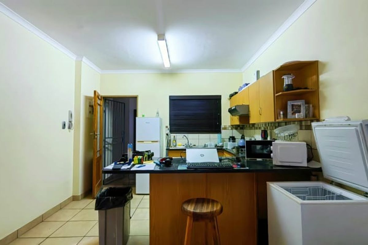 A functional kitchen area featuring built-in wooden cabinetry, laminate countertops, a stainless steel sink, and tiled flooring.