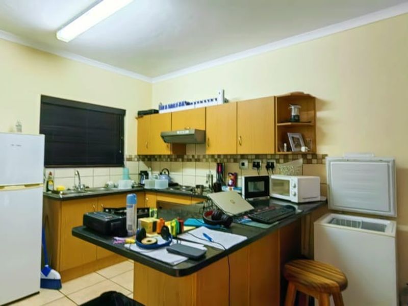 A functional kitchen featuring laminate cabinetry, dark countertops, a tiled backsplash, and an integrated extractor fan, offering potential for modern cosmetic updates.