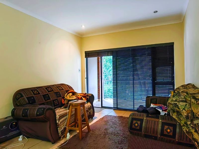 A living room featuring tiled flooring, recessed lighting, and a sliding glass door with venetian blinds leading to an outdoor area.
