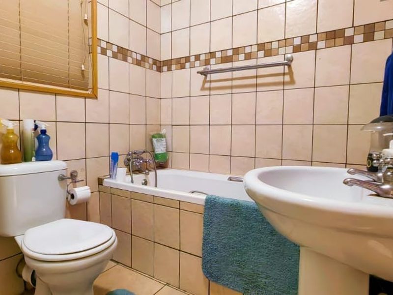 A functional bathroom featuring a bathtub, pedestal basin, and toilet with neutral wall tiling and a window for natural light.