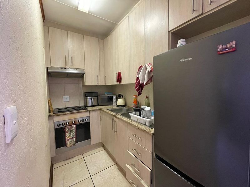 Compact kitchen featuring light wood-finish cabinetry, laminate countertops, built-in oven, electric hob, and tiled flooring.