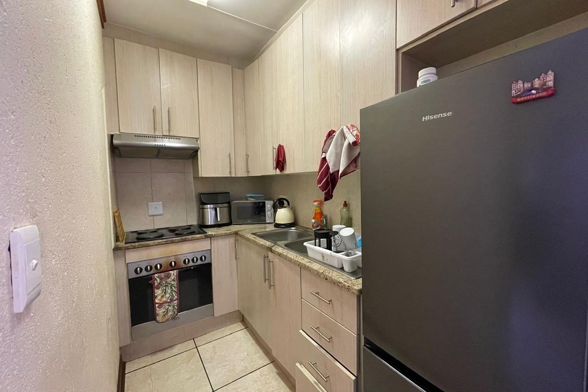 Compact kitchen featuring light wood-finish cabinetry, laminate countertops, built-in oven, electric hob, and tiled flooring.