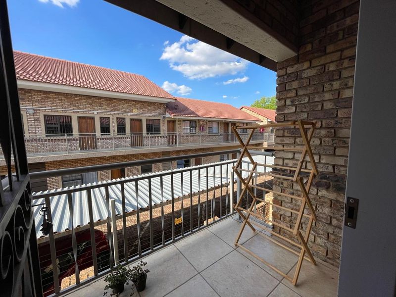 A covered balcony featuring tiled flooring, a brick feature wall, and a metal balustrade overlooking the apartment complex courtyard.