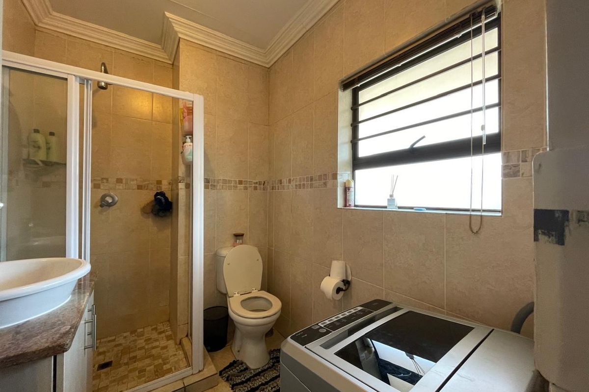 A functional bathroom featuring a shower enclosure, toilet, and vanity basin with neutral wall and floor tiling, providing a practical layout for daily use.