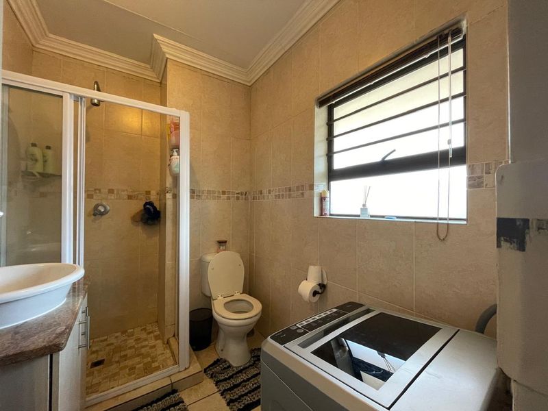 A functional bathroom featuring a shower enclosure, toilet, and vanity basin with neutral wall and floor tiling, providing a practical layout for daily use.