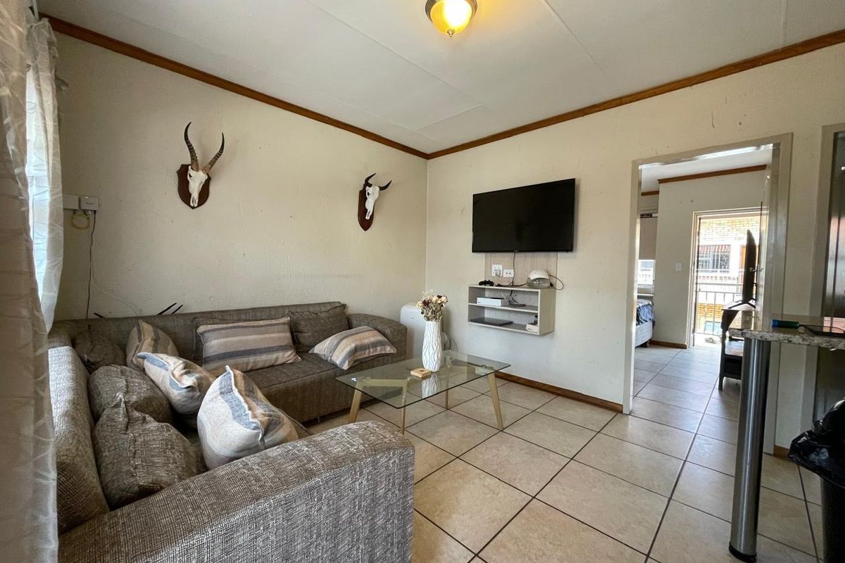 A living room featuring tiled flooring and wall-mounted shelving, providing a functional space with direct access to an adjacent room.