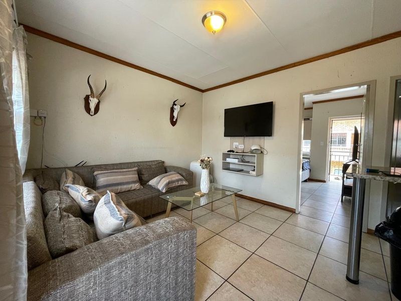 A living room featuring tiled flooring and wall-mounted shelving, providing a functional space with direct access to an adjacent room.