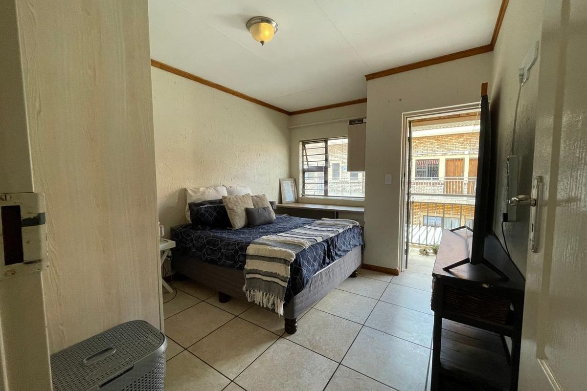 A functional bedroom featuring tiled flooring, louvered windows, and direct access to a private balcony.