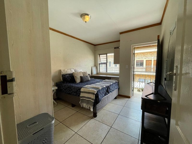 A functional bedroom featuring tiled flooring, louvered windows, and direct access to a private balcony.