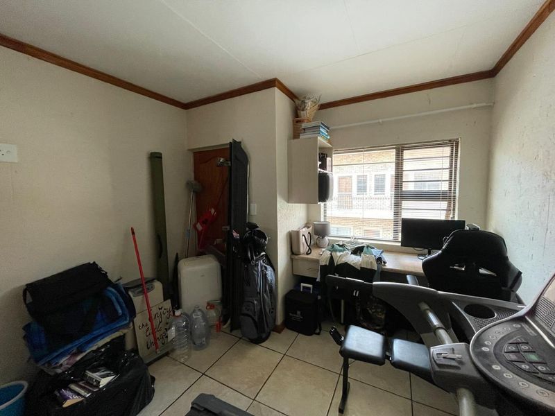 A compact bedroom featuring tiled flooring, a built-in desk, and integrated shelving, currently utilized as a multi-purpose workspace and storage area.