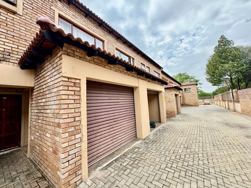 Exterior view of a residential apartment complex featuring multiple brick-faced garages with roller shutter doors and a paved driveway.
