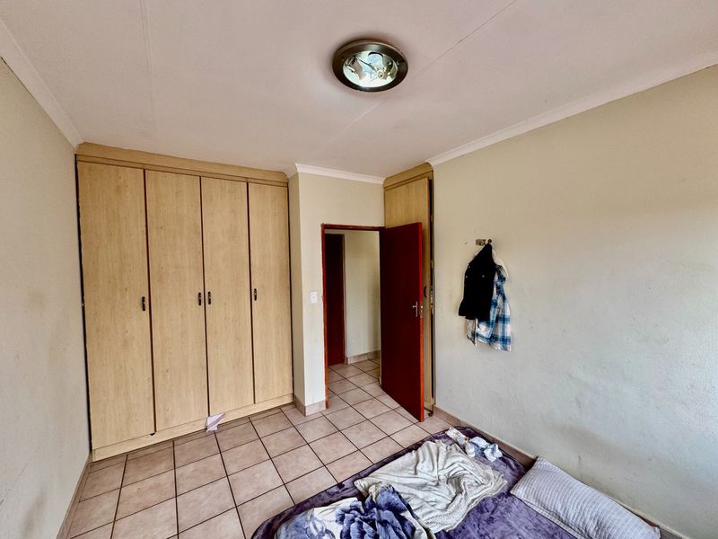 A bedroom featuring built-in wooden cupboards, tiled flooring, and a central ceiling light fixture, offering a functional space with potential for cosmetic updates.