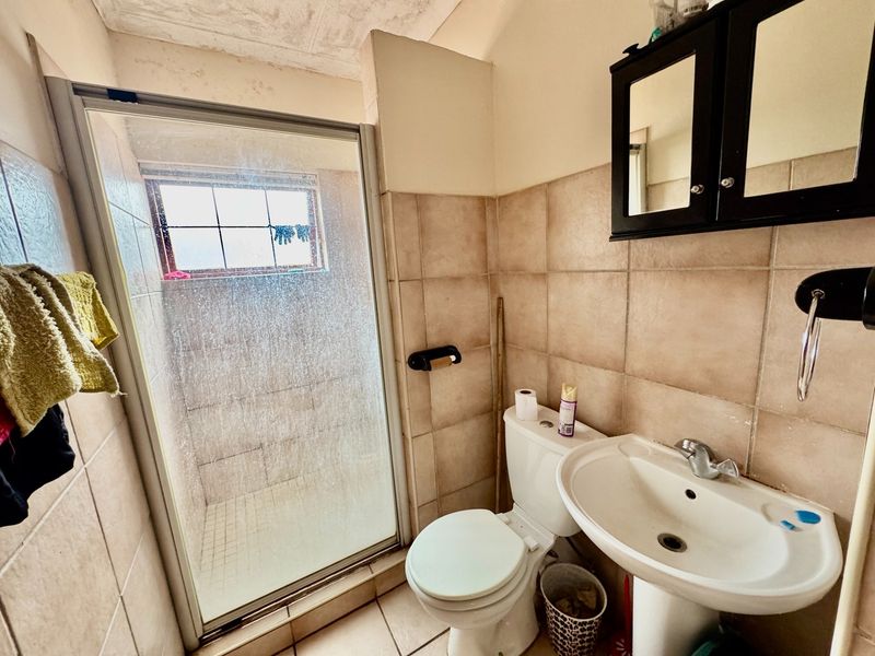 Compact bathroom featuring a shower enclosure, pedestal basin, and toilet with neutral wall tiling. The space would benefit from cosmetic updates and maintenance.