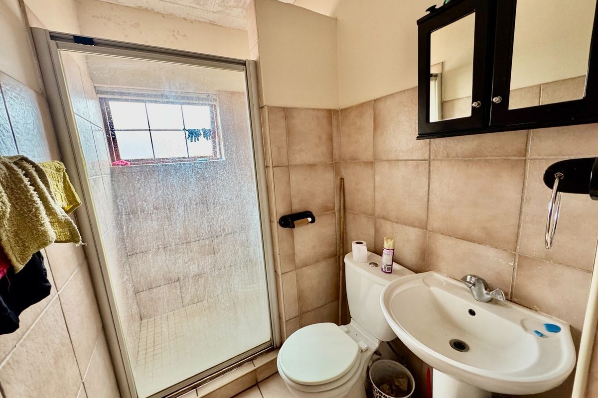 Compact bathroom featuring a shower enclosure, pedestal basin, and toilet with neutral wall tiling. The space would benefit from cosmetic updates and maintenance.