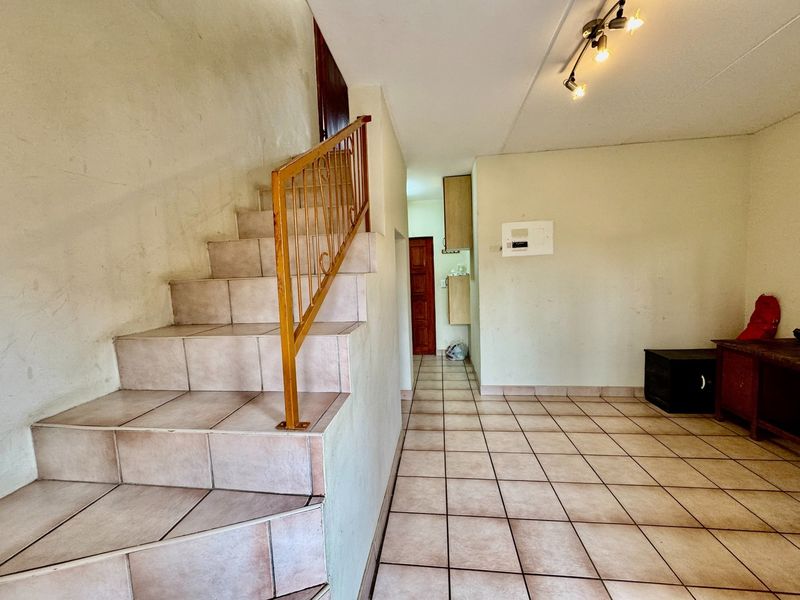 An open-plan living area featuring tiled flooring, a staircase with a metal balustrade, and neutral wall finishes, presenting a blank canvas for renovation.