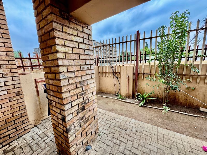 A private outdoor patio area featuring paved flooring, a brick support pillar, and secure perimeter fencing, offering a functional space for outdoor use.