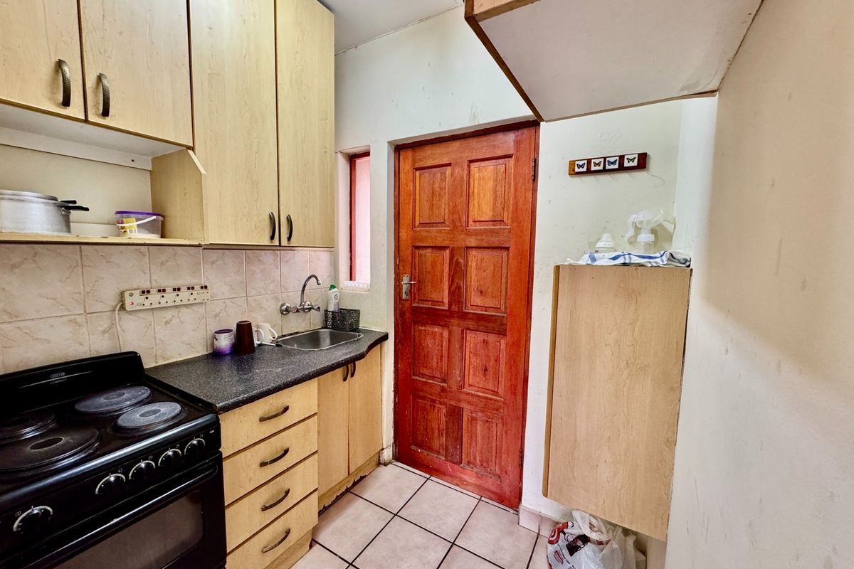 A compact kitchen featuring built-in wooden cabinetry, laminate countertops, a stainless steel sink, and an electric stove with tiled backsplash and flooring.