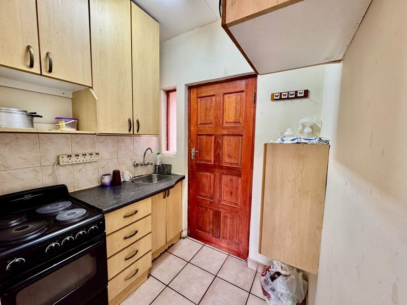 A compact kitchen featuring built-in wooden cabinetry, laminate countertops, a stainless steel sink, and an electric stove with tiled backsplash and flooring.
