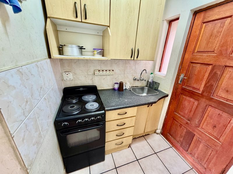 Compact kitchen featuring built-in cabinetry, a stainless steel sink, tiled splashback, and a freestanding stove, providing a functional preparation area.