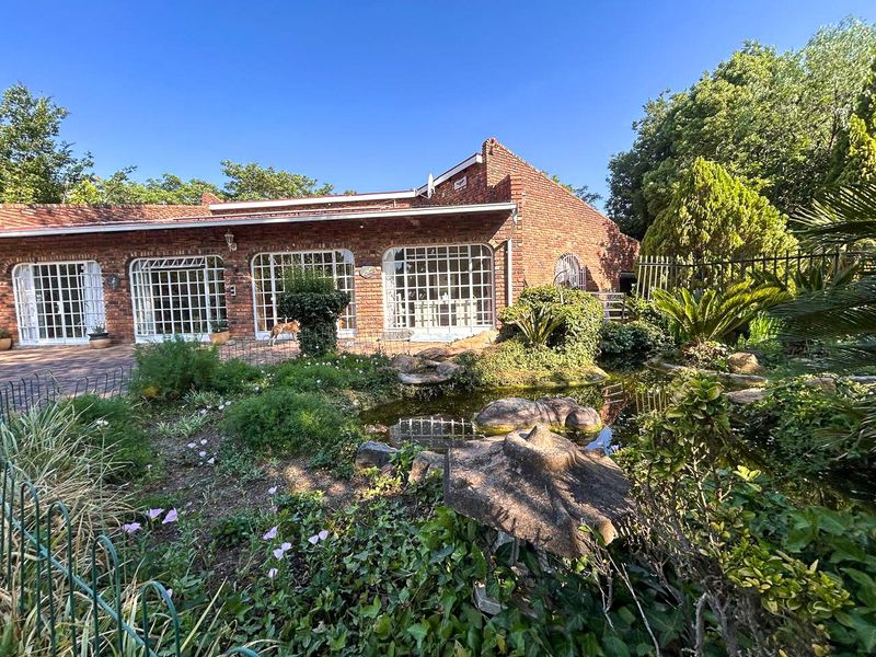 Rear view of a brick house featuring large grid-pattern windows, a landscaped garden, and a decorative pond.