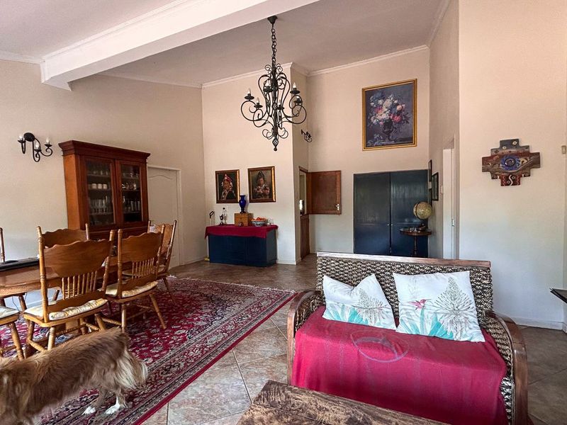 Spacious open-plan living and dining area featuring high ceilings with exposed beams, tiled flooring, and a classic wrought iron chandelier.