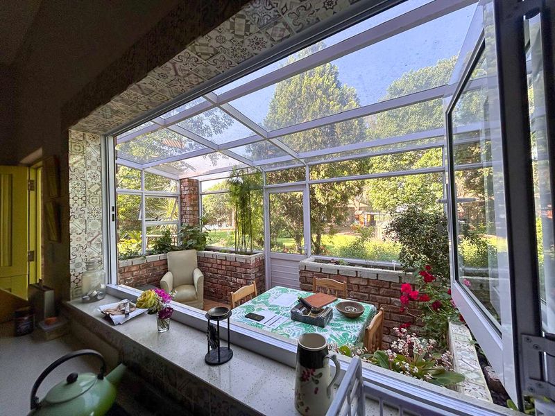 A bright, enclosed sunroom or patio area featuring brick planter boxes, large glass windows, and decorative tiled accents overlooking the garden.