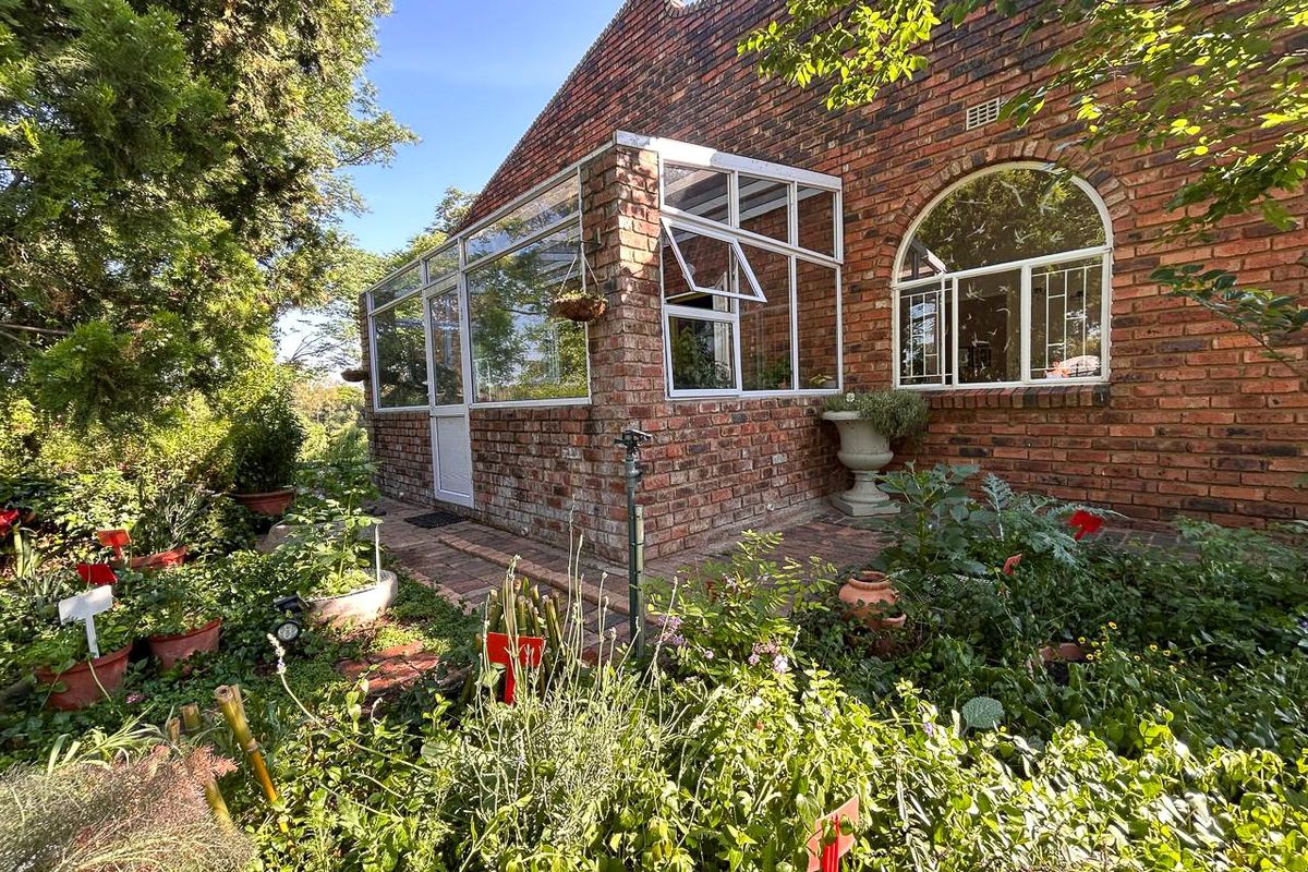A charming rear exterior view featuring a face brick facade, a sunroom extension, and an arched window overlooking a lush garden.