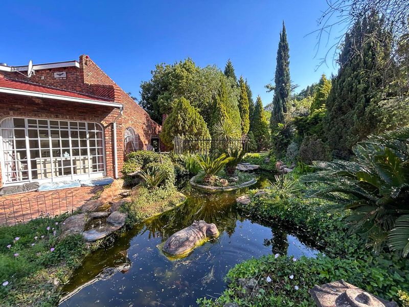 A lush, landscaped garden featuring a decorative pond, mature trees, and a brick-paved patio area adjacent to the home's exterior.