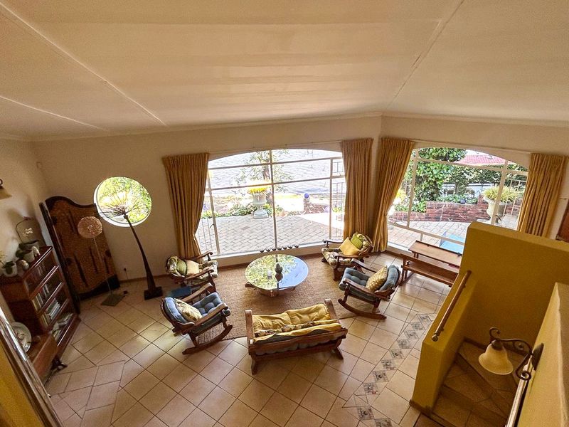 Spacious living area featuring large arched windows with garden views, tiled flooring, and a staircase leading to the upper level.