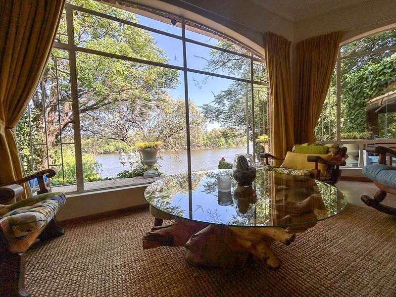 A bright living area featuring expansive steel-framed windows that offer scenic views of the surrounding trees and water.