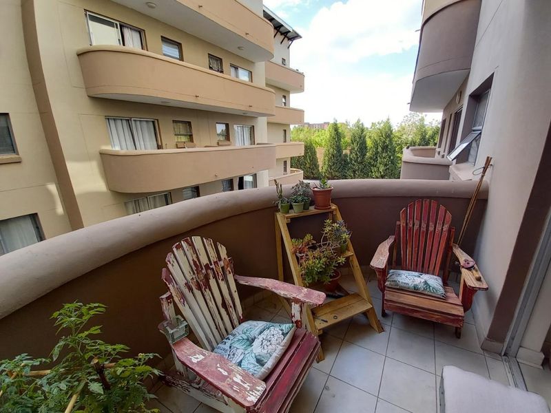 A private apartment balcony featuring tiled flooring and a curved masonry balustrade, overlooking the surrounding residential complex.