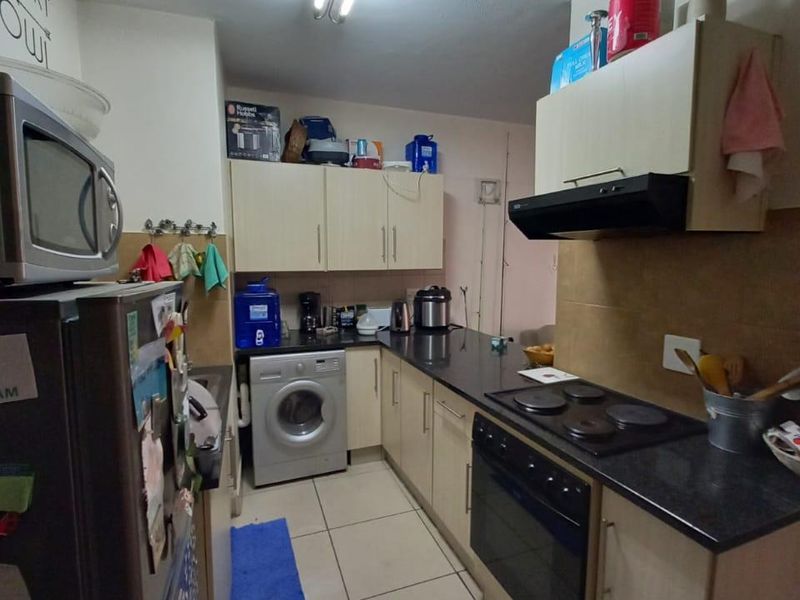 A functional galley-style kitchen featuring built-in cabinetry, an electric hob, oven, extractor fan, and tiled flooring.
