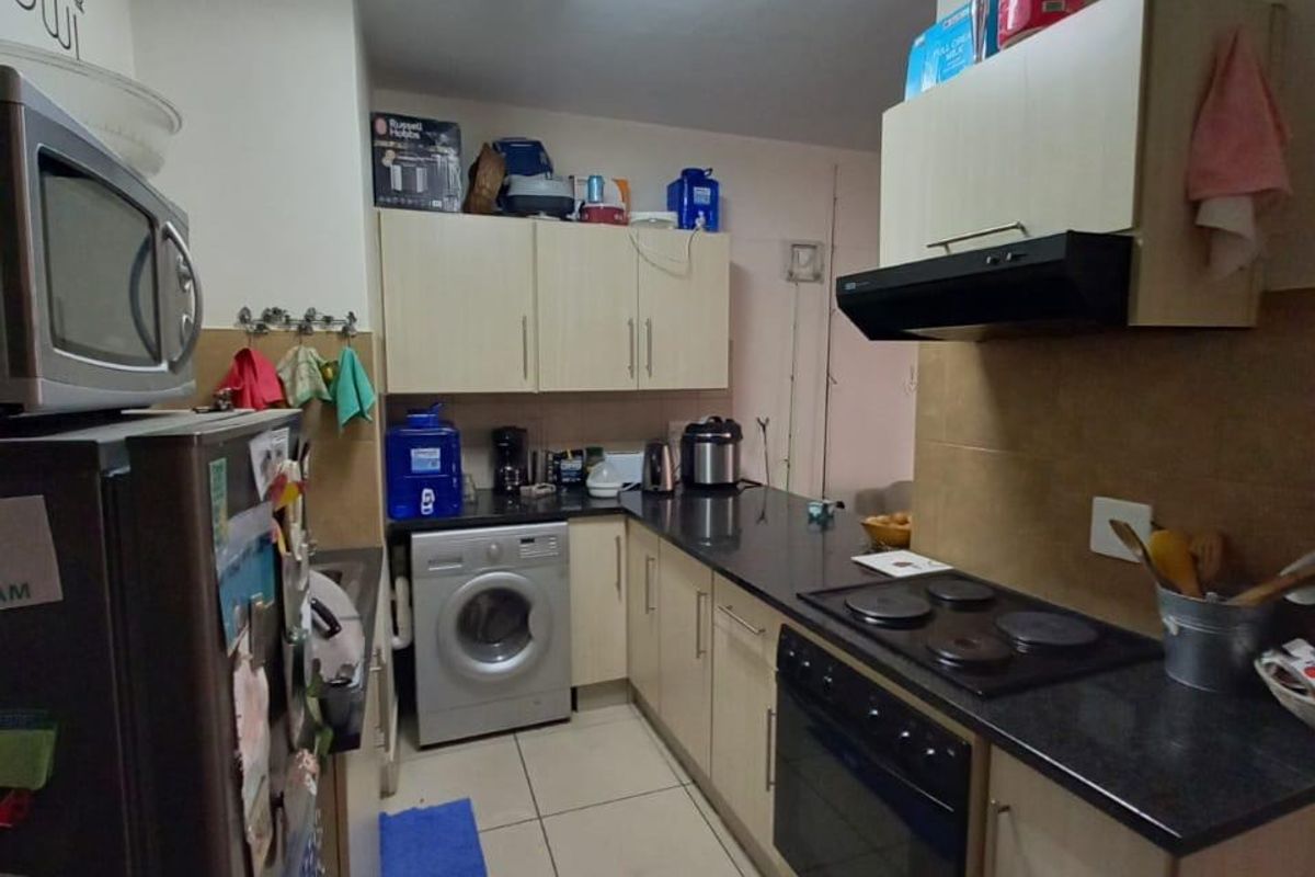 A functional galley-style kitchen featuring built-in cabinetry, an electric hob, oven, extractor fan, and tiled flooring.