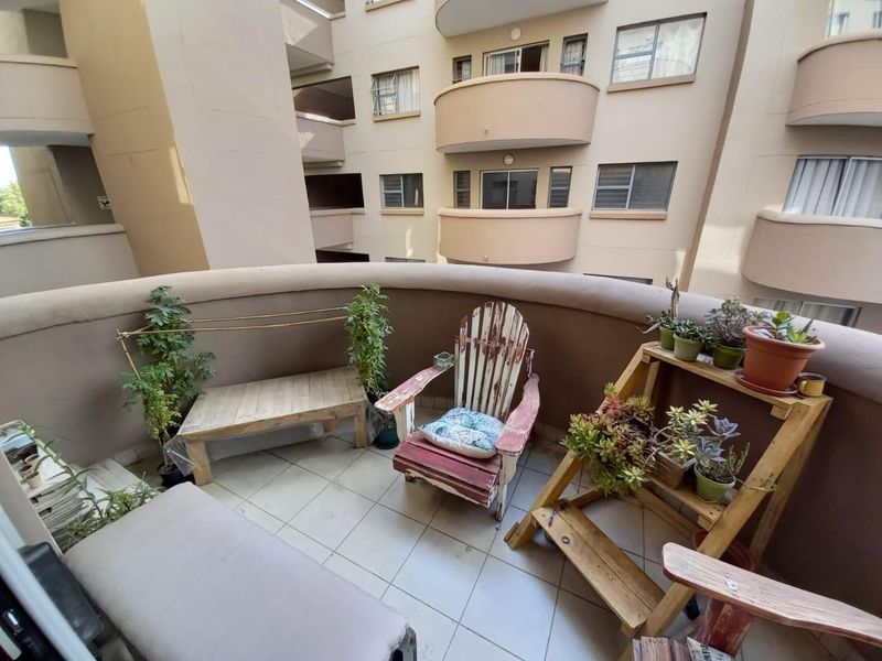 A private apartment balcony featuring tiled flooring and a curved masonry balustrade, overlooking the building's central courtyard area.
