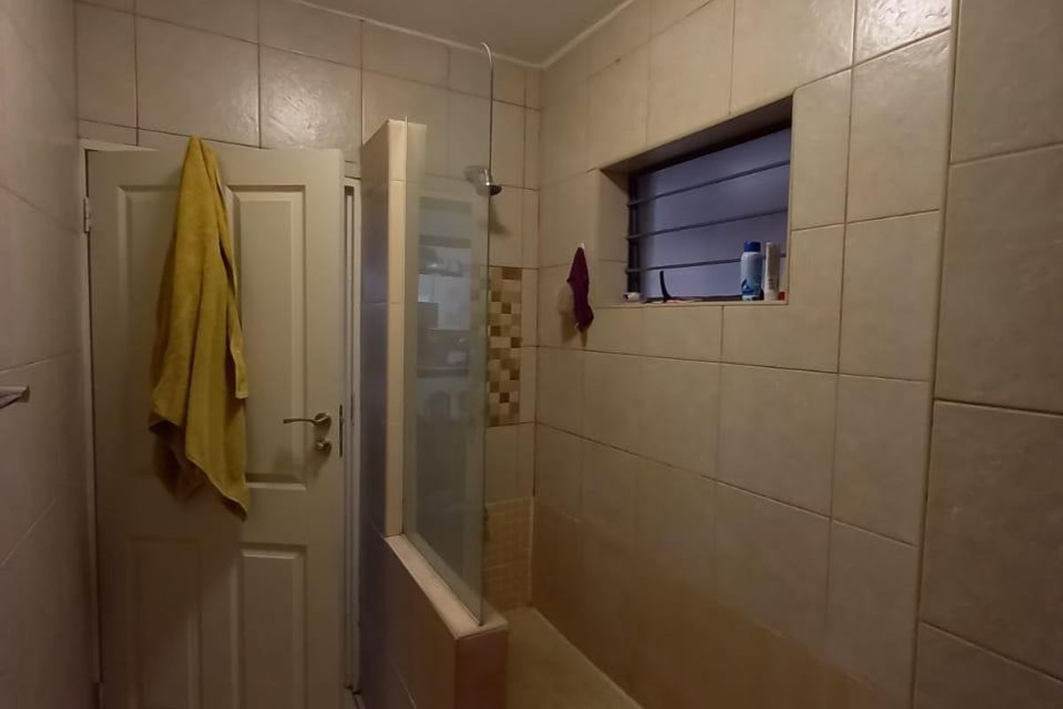 A functional bathroom featuring a walk-in shower with a glass screen and neutral wall tiling.