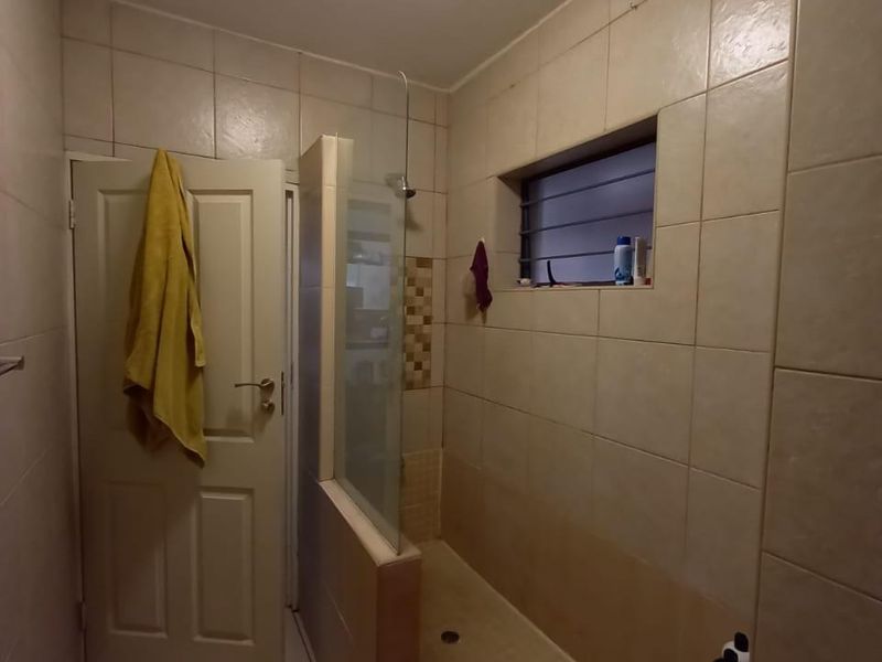 A functional bathroom featuring a walk-in shower with a glass screen and neutral wall tiling.