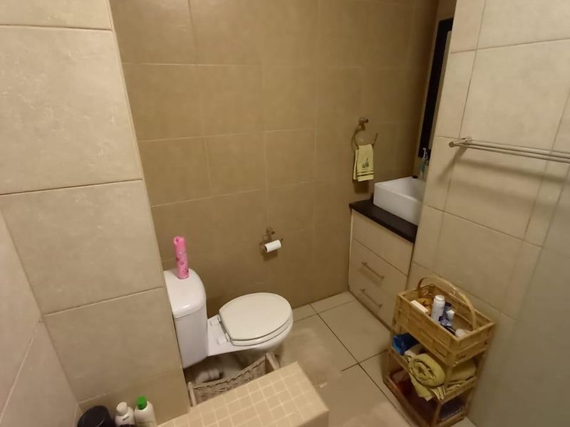 A compact bathroom featuring a vanity with a vessel sink, a toilet, and a tiled shower base with neutral wall tiling.