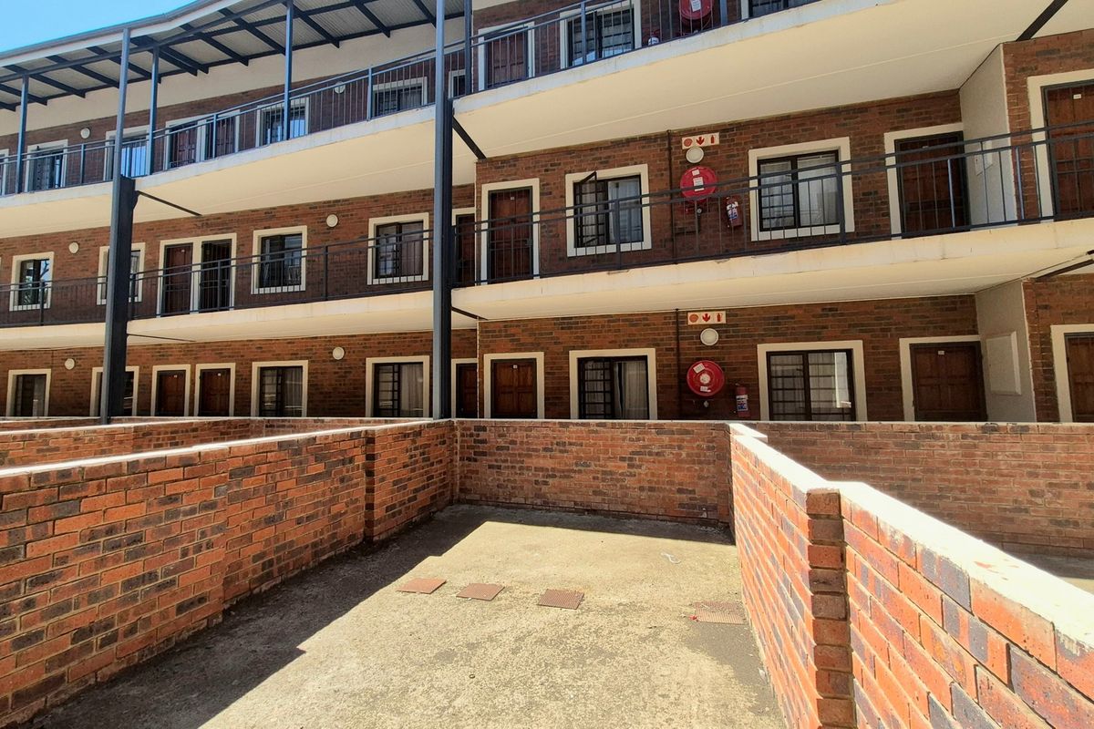 Exterior view of a multi-story apartment complex featuring face brick construction, private ground-level patio areas, and metal balcony railings.