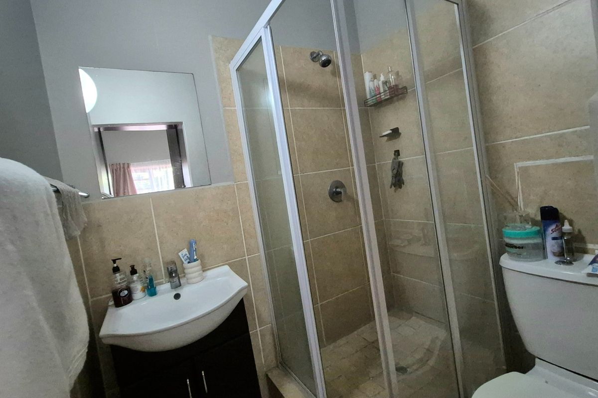 A functional bathroom featuring a glass-enclosed shower, vanity basin with storage cabinet, and a standard toilet with neutral wall tiling.