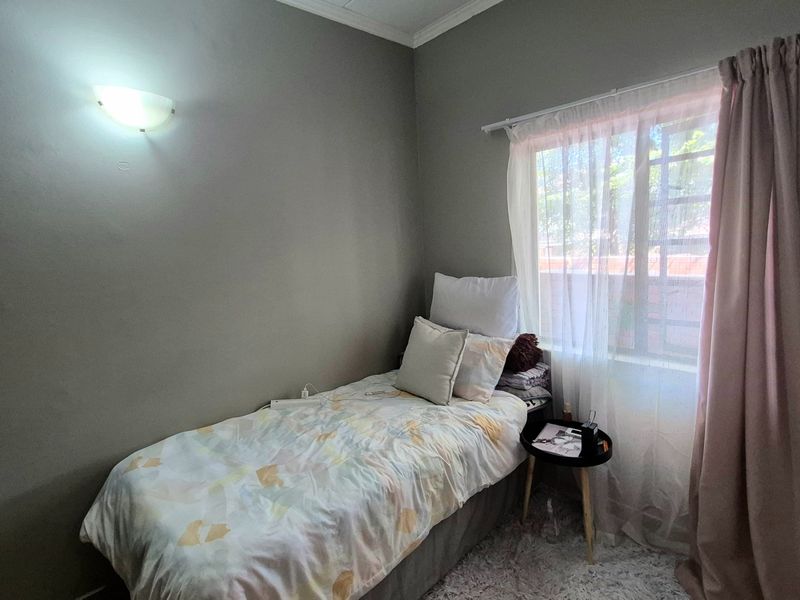A compact bedroom featuring neutral wall tones, a window with security bars, and a wall-mounted light fixture.
