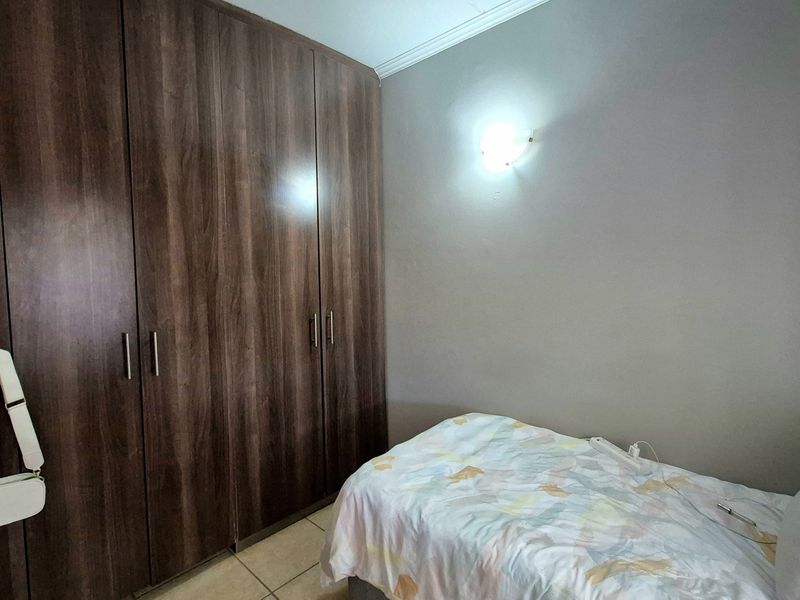 A bedroom featuring dark wood-finish built-in cupboards, tiled flooring, and a wall-mounted light fixture.