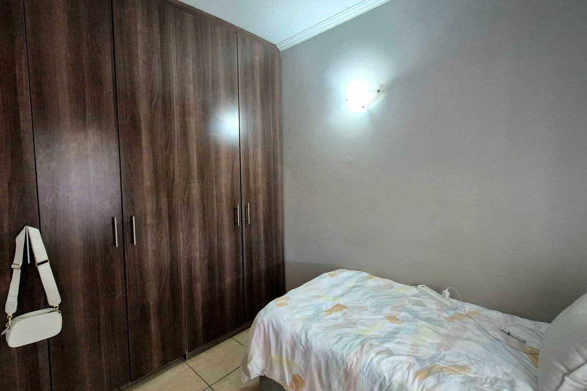 A bedroom featuring dark wood-finish built-in cupboards, tiled flooring, and a wall-mounted light fixture.