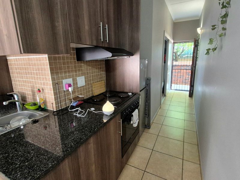 Compact galley-style kitchen featuring dark wood cabinetry, granite countertops, built-in oven and hob, and tiled flooring leading to an exterior security gate.
