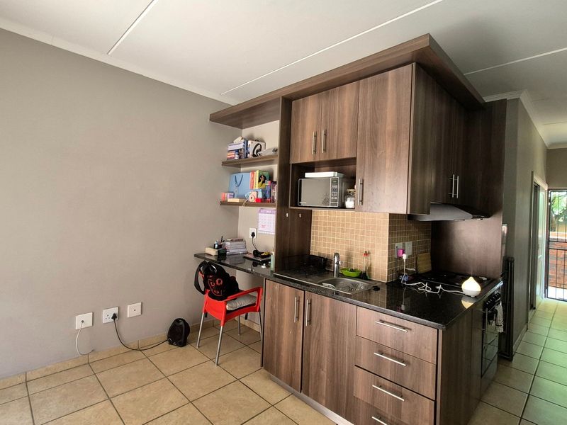 Compact kitchen featuring dark wood cabinetry, granite countertops, built-in oven and hob, and a tiled backsplash, with an integrated workspace area.