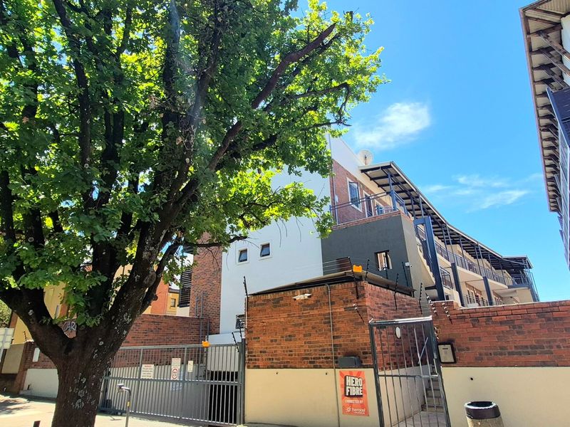 Exterior view of the apartment complex featuring a brick boundary wall, secure gated entrance, and multi-story building facade with balconies.
